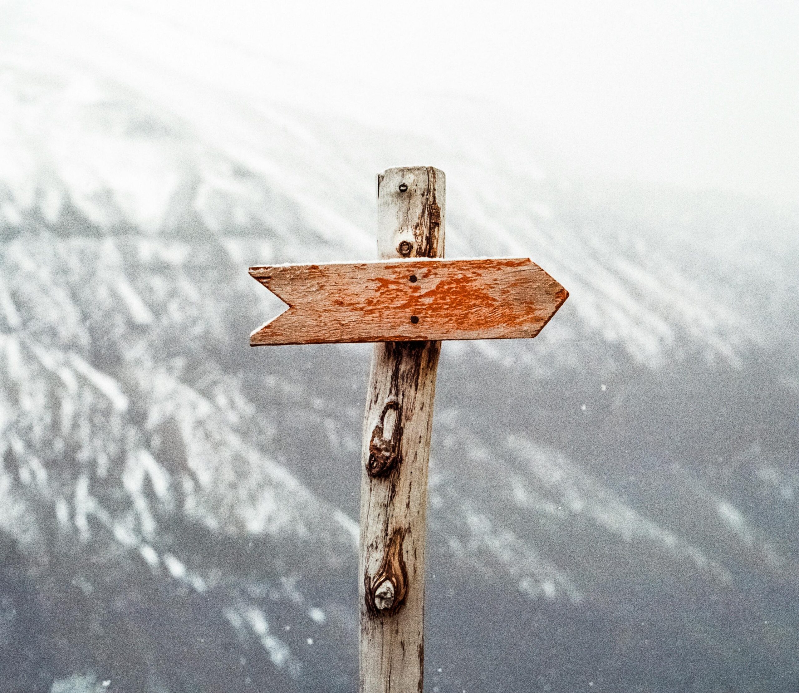 A wooden arrow signpost points the way amidst a snowy mountain landscape.